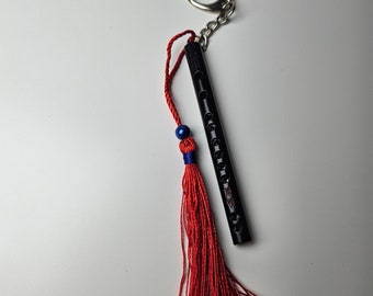 Può includere: Un flauto in legno nero con portachiavi, nappa rossa e perline blu. Il flauto ha un portachiavi argentato.