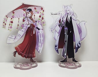 Könnte beinhalten: Zwei Acryl-Ständer mit Anime-Charakteren. Der Ständer links zeigt eine weibliche Figur mit langen braunen Haaren, die ein weißes und rotes Kimono mit einem rosa und weißen Regenschirm trägt. Der Ständer rechts zeigt eine männliche Figur mit langen weißen Haaren, die ein weißes und schwarzes Kimono trägt. Beide Ständer haben eine rosa und weiße Basis.