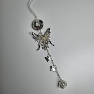 May include: Silver butterfly charm with a chain and smaller butterfly charms hanging from it. The charm is attached to a white string.