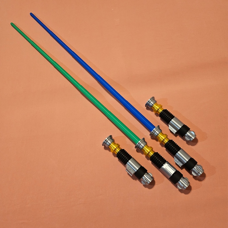 May include: Three lightsaber toys, one green, one blue, and one silver with gold accents. The lightsabers are laid out on a pink surface.