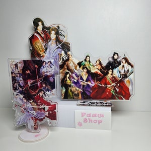 以下が含まれることがあります： カラフルな服とアクセサリーをつけたアニメキャラクターが描かれたアクリル製キャラクタースタンドのセット。スタンドは、ピンクの「Paw Shop」と書かれた白い表面に飾られています。