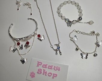May include: A set of silver jewelry featuring butterfly and moon charms. The set includes a bracelet, a necklace, a bangle, and earrings. The jewelry is accented with red and blue gemstones.