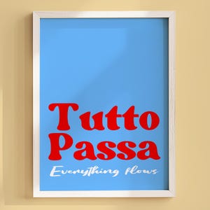 以下が含まれることがあります： 明るい青色の背景に、赤い文字で「Tutto Passa」、その下に「Everything flows」と書かれた額入りのアートプリント。 フレームは白で、作品はベージュ色の壁に飾られています。