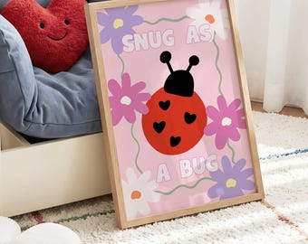 Puede incluir: Un cuadro rectangular con marco y fondo rosa claro que muestra una mariquita roja con manchas negras en forma de corazón y antenas negras. La lámina incluye el texto SNUG AS A BUG y está decorada con flores de color morado, rosa y blanco.