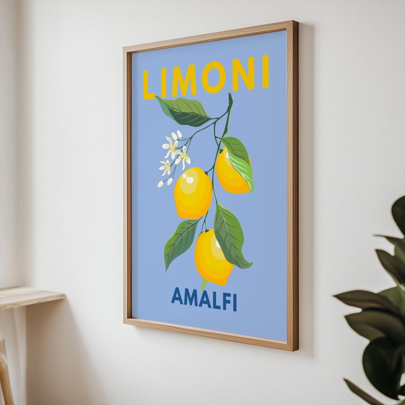 May include: A framed art print featuring a branch of lemons with green leaves and white blossoms against a light blue background. The word "LIMONI" is in yellow above the lemons, and "AMALFI" is in blue below.