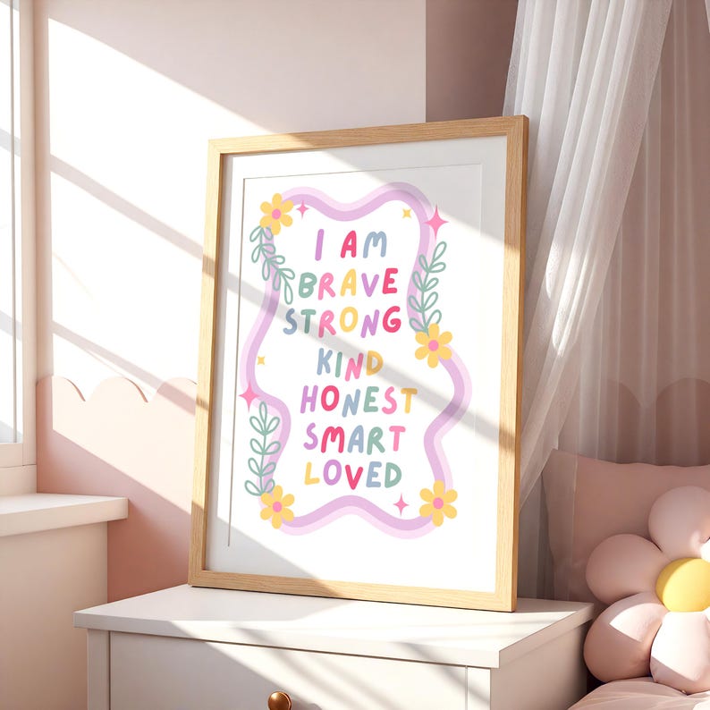 May include: A framed print with the words "I AM BRAVE STRONG KIND HONEST SMART LOVED" in colorful text. The print has a light wood frame and is decorated with floral and leaf accents. The background is white.
