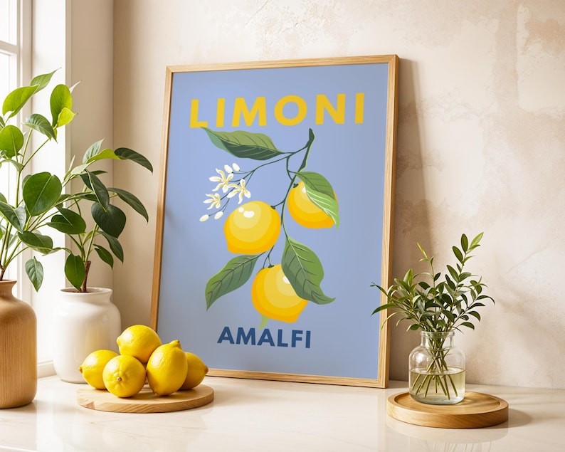 May include: A framed art print featuring a lemon branch with yellow lemons, green leaves, and white blossoms against a light blue background. The word "LIMONI" is at the top, and "AMALFI" is at the bottom. The frame is light brown.