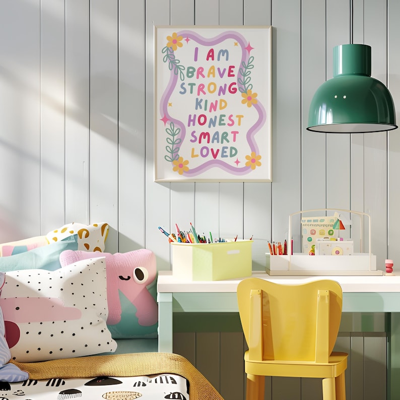 May include: A framed print with the words "I AM BRAVE STRONG KIND HONEST SMART LOVED" in colorful text. The print hangs above a desk with a yellow chair. Other items include pillows, a green lamp, and a container of pencils.