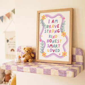 May include: A framed print with the words "I AM BRAVE STRONG KIND HONEST SMART LOVED" in colorful letters. The print is on a shelf with a checkerboard pattern, next to a teddy bear and a duck figurine. The shelf is mounted on a white wall.