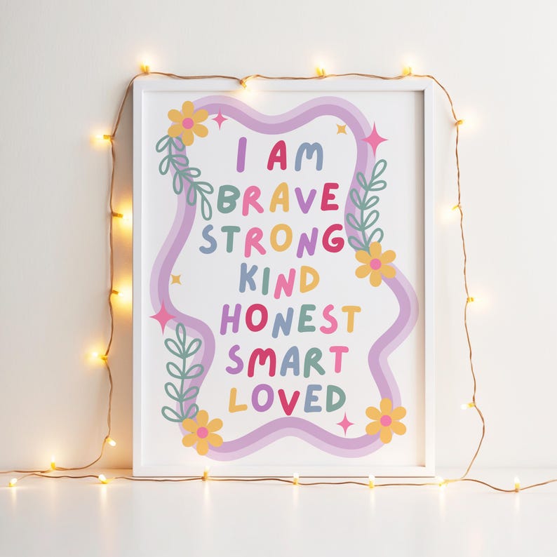 May include: A framed art print with the words "I AM BRAVE STRONG KIND HONEST SMART LOVED" in colorful letters. The design includes a wavy purple border, flowers, and leaves. The frame is white, and the background is a light color.