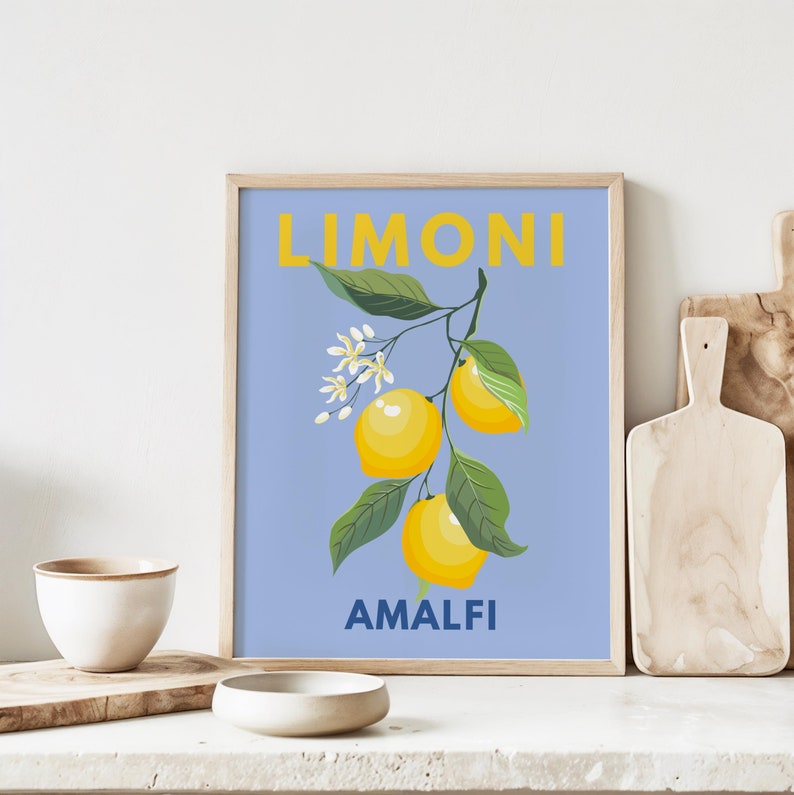 May include: A framed art print featuring a branch of lemons with green leaves and white blossoms against a light blue background. The word "LIMONI" is printed in yellow at the top, and "AMALFI" is printed in blue at the bottom.