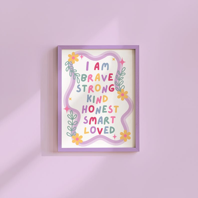 May include: A framed art print with a purple border. The print features the words "I AM BRAVE STRONG KIND HONEST SMART LOVED" in colorful, playful lettering. Floral and leaf accents surround the text on a white background.