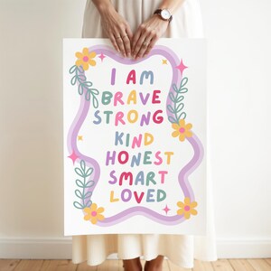 May include: A white poster with the words "I AM BRAVE STRONG KIND HONEST SMART LOVED" in colorful letters. The words are framed by a wavy purple border, flowers, and leaves.