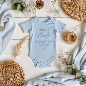 May include: A light blue baby onesie with the text "PRIMER NIETO EN CAMINO JUNIO 2025" and a small heart.