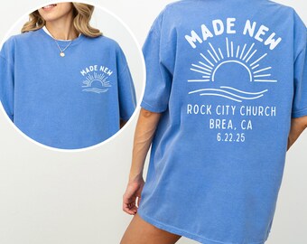 May include: Flo blue short-sleeved t-shirt with white graphic text and design. The front of the shirt has "MADE NEW" above a sun and wave design. The back of the shirt has the same design with "ROCK CITY CHURCH BREA, CA 6.22.25".