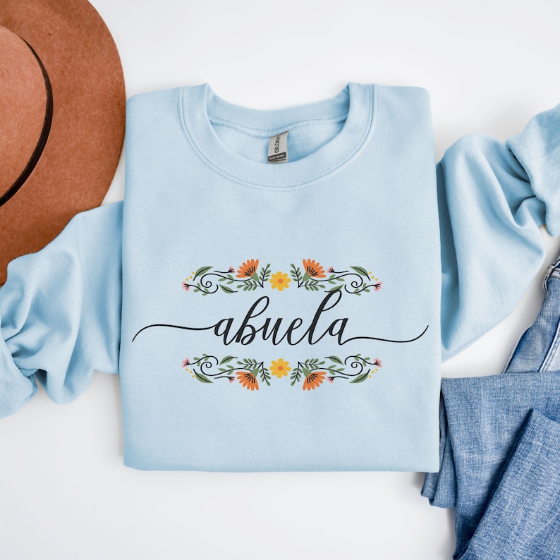 May include: A light blue sweatshirt with a floral design and the word "abuela" in black script.