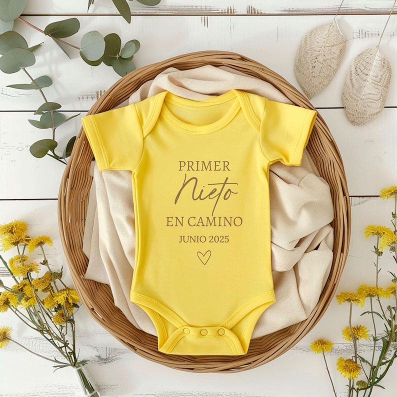 May include: Yellow baby onesie with the text "PRIMER NIETO EN CAMINO JUNIO 2025" in brown lettering and a small heart.