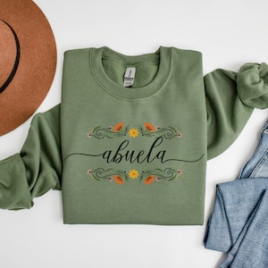 May include: A green sweatshirt with the word "abuela" in black script surrounded by a floral design with orange and yellow flowers.