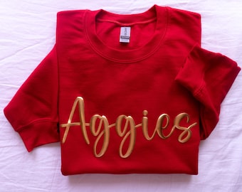 May include: Red sweatshirt with the word "Aggies" in gold lettering.