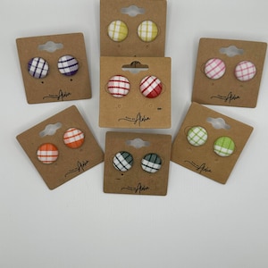 May include: Assortment of 10 pairs of small, round, fabric earrings with a plaid pattern. The earrings are displayed on brown card stock with the words "Pure Aloha" printed on each card. The earrings are in the following colors: purple, red, yellow, pink, orange, green, and black.