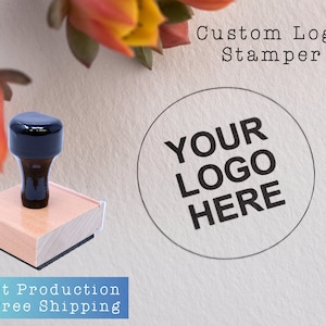 May include: A wooden self-inking stamp with a black rubber stamp pad. The stamp is rectangular and has a round impression area. The impression area says "YOUR LOGO HERE". The stamp is on a white surface with the text "Custom Logo Stamper" above it.