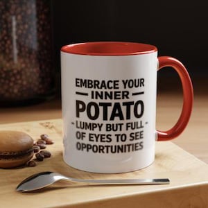 May include: White ceramic mug with a red rim and handle. The mug has black text that reads "Embrace your inner potato - Lumpy but full of eyes to see opportunities".