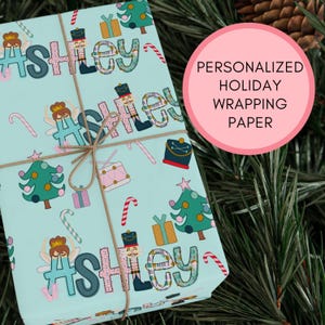 May include: Personalized holiday wrapping paper with a blue background and a repeating pattern of Christmas trees, candy canes, nutcrackers, and the name "Ashley".