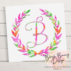 May include: A floral wreath design with a large letter "B" in the center. The wreath and letter feature pink, orange, and green floral patterns. The text "Blush Bunny Design" is written in cursive below the wreath.