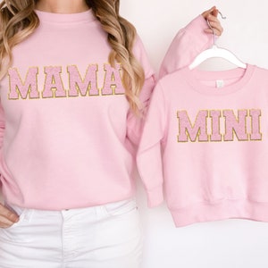 May include: Pink sweatshirts with gold glitter lettering. The larger sweatshirt says "MAMA" and the smaller sweatshirt says "MINI".