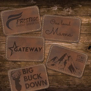May include: A collection of five brown leatherette patches with various designs and text. One patch reads "PRESTIGE EVENT SERVICES", another says "One loved Mama", and others feature a star, mountain range, and a deer with "BIG BUCK DOWN".