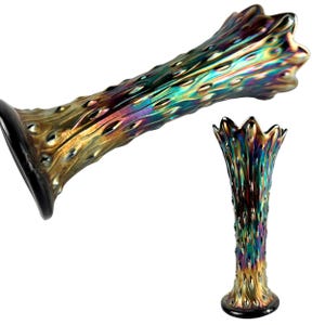 May include: A tall, slender glass vase featuring an iridescent, multi-colored finish with shifting hues of gold, green, and purple. The surface is covered in a repeating pattern of raised, textured bumps, and the top rim has a scalloped edge.