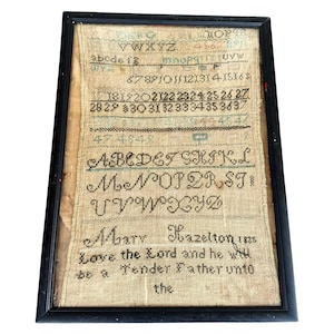 May include: Framed antique sampler with black wooden frame. The sampler features embroidered letters, numbers, and the name "Mary Hazelton 1825." The text includes "Love the Lord and he will be a Tender Father unto the."