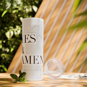 Op de afbeelding: Een witte tumbler met een zwart-witte print die "YES & AMEN" zegt. De tumbler staat op een houten oppervlak met groene bladeren.