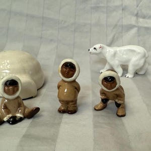 Op de afbeelding: Een set van vijf keramische beeldjes die een iglo, een ijsbeer en drie mensen in traditionele Inuit-kleding voorstellen. De beeldjes zijn geschilderd in tinten wit, bruin en zwart.