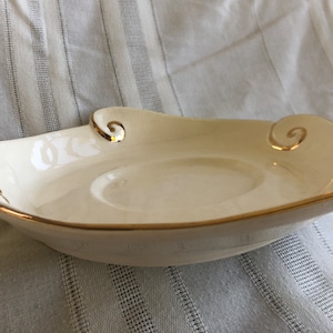 May include: A white ceramic saucer with a gold rim and decorative swirls. The saucer is designed for a teacup or coffee cup.
