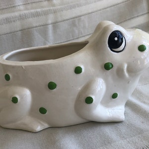 May include: White ceramic frog planter with green polka dots. The frog has a large, black eye and a wide, open mouth.