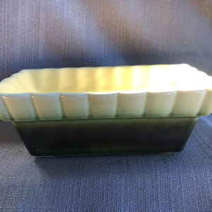 Peut inclure: Un pot de fleurs rectangulaire en céramique avec un glaçage vert et jaune. Le pot a un motif cannelé autour du bord supérieur.