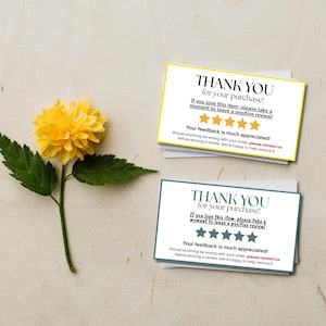 May include: Two rectangular thank you cards with black text and five stars, one with a yellow border and one with a teal border, accompanied by a bright yellow flower with green leaves on a light wood grain surface.