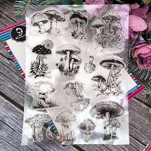 Peut inclure: Un ensemble de tampons transparents avec des illustrations de champignons à l'encre noire. Les motifs présentent diverses variétés de champignons, avec des chapeaux et des tiges détaillés, certains avec du feuillage. Idéal pour les projets créatifs.