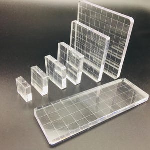 Op de afbeelding: Een verzameling heldere acrylblokken van verschillende afmetingen, elk geëtst met een rasterpatroon. De blokken zijn gerangschikt in aflopende grootte, wat hun transparantie en geometrische ontwerp benadrukt. Ideaal voor knutselen of tentoonstelling.