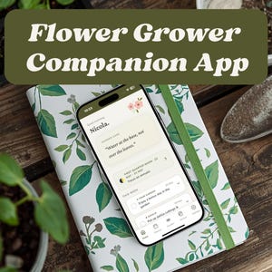 May include: A smartphone displaying the Flower Grower Companion App interface, featuring a personalized greeting for Nicola, gardening tips, and task lists, resting on a white notebook with a green leaf pattern and a green elastic closure band.
