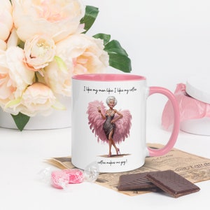 May include: White ceramic coffee mug with a pink rim and handle. The mug features a cartoon illustration of a woman in a pink feather boa and the text "I like my man like I like my coffee coffee makes me gay!"