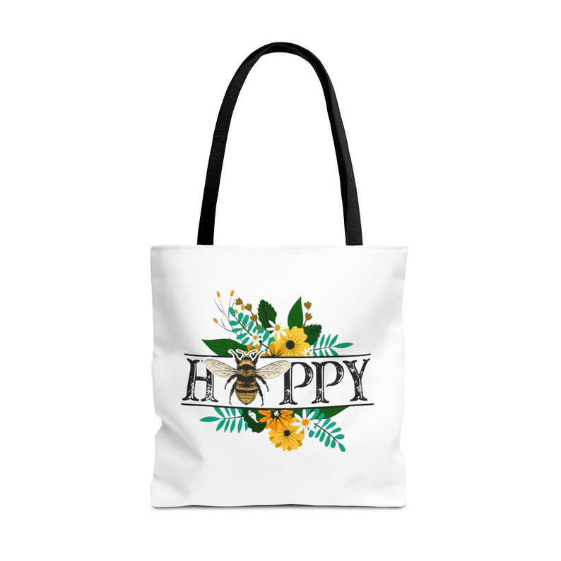 May include: White tote bag with a black handle and a floral design featuring a bee and the word "HAPPY".