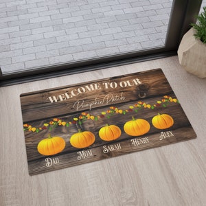 May include: A rectangular doormat with a wooden background. The mat reads "WELCOME TO OUR Pumpkin Patch" in white script. Five orange pumpkins are featured, each with a family member's name below.