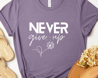 May include: Purple t-shirt with the text "NEVER give up" in white lettering. A white dandelion with seeds blowing away is below the text.
