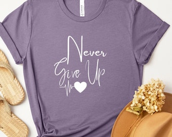 May include: Purple t-shirt with the text "Never Give Up" in white cursive lettering with a white heart and a heartbeat graphic.