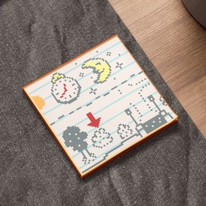 May include: A small, square, orange-brown card with a pixelated design of a clock, a moon, and a downward arrow. The card has a white background with blue lines and is on a gray surface.