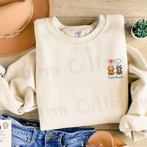 May include: A beige sweatshirt with a pixelated design of three cats and a heart. The text "Tsuki Munch" is below the design.