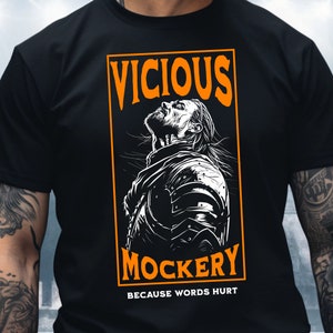 Può includere: Maglietta nera con una grafica bianca di un uomo in armatura con il testo "VICIOUS MOCKERY BECAUSE WORDS HURT" in arancione.