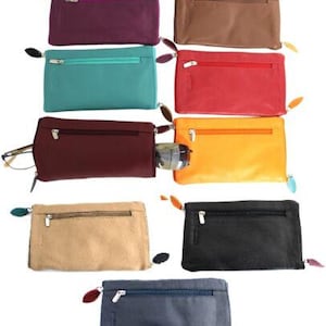 May include: A collection of nine rectangular leather pouches in various colors including purple, brown, teal, red, maroon, yellow, beige, black, and navy blue. Each pouch features a horizontal zippered front pocket and a silver-toned zipper pull.